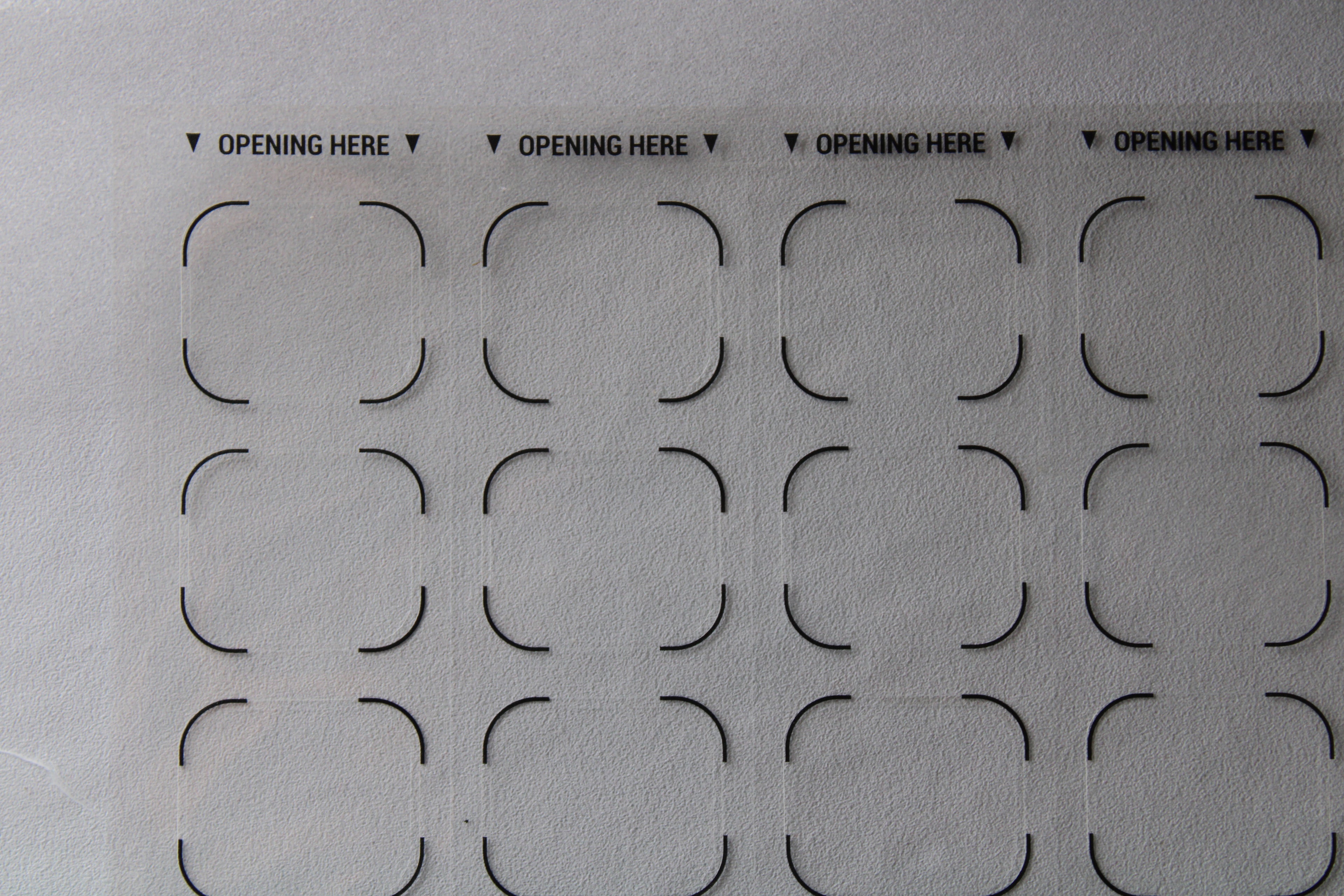 Sheet of pre-cut cardboard shapes with 'OPENING HERE' text on a gray background. Correction labels for pharmacy blister packaging and medication labeling